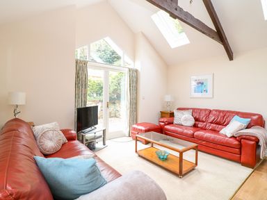 A living room with red leather sofas a glass coffee table a television and large windows at FernGully in St Columb Major