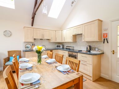 A kitchen with wooden cabinets and a dining table set with plates and flowers at FernGully in St Columb Major