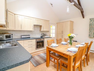 A kitchen with wooden cabinets a countertop a dining table with six chairs and a vase of flowers at FernGully in St Columb Major