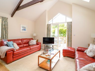 A living room with red leather sofas a glass coffee table and a television by a door at FernGully in St Columb Major