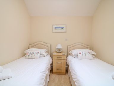 A bedroom with two single beds and a nightstand with a lamp at FernGully in St Columb Major