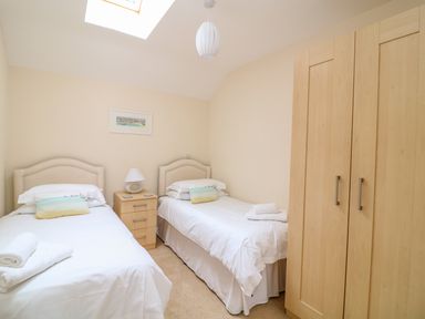 A bedroom with two single beds a nightstand a lamp and a wardrobe at FernGully in St Columb Major