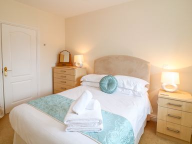 A bedroom with a bed covered with white and light blue linens and two bedside tables with lamps at FernGully in St Columb Major