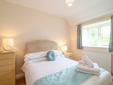 A bedroom with a double bed bedside tables with lamps and a window with curtains at FernGully in St Columb Major