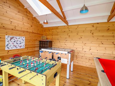 A game room with foosball table pool table and small cabinet with a bird poster on the wooden wall at FernGully in St Columb Major