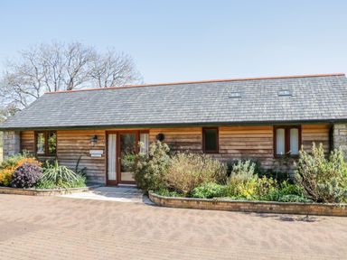 A wooden house with a gray slate roof and planted shrub beds at Kingcup Cottage in St Columb Major