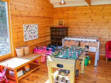 A game room with a foosball table a table with baskets toys and a poster on wooden walls at Kingcup Cottage in St Columb Major