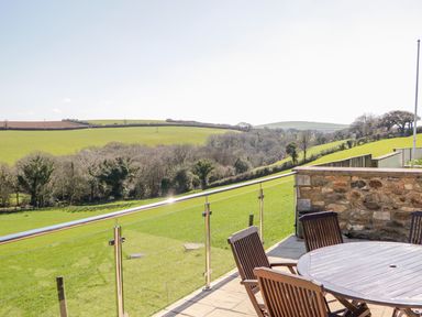 An outdoor patio with a round wooden table and chairs overlooking green fields at Kingcup Cottage in St Columb Major