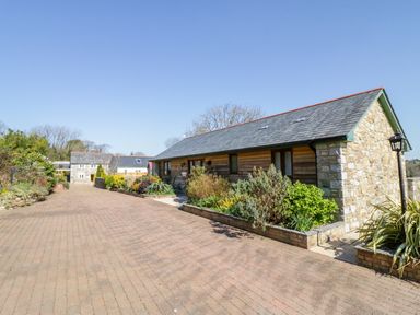 An outdoor paved driveway with stone and wooden buildings and garden beds at Kingcup Cottage in St Columb Major