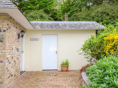 An outdoor area with a white door labeled laundry next to a brick wall and surrounded by green bushes at Kingcup Cottage in St Columb Major