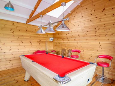 A game room with a red pool table wooden walls three hanging lights and red bar stools at Kingcup Cottage in St Columb Major