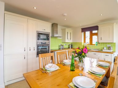 A kitchen with a dining table set for six and green tiled backsplash at Kingcup Cottage in St Columb Major
