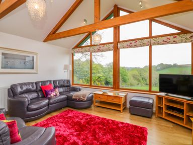 A living room with leather sofas a red rug wooden furniture and large windows showing a countryside view at Kingcup Cottage in St Columb Major
