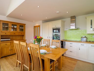 A kitchen and dining area with a wooden table set for six and wooden cabinets at Kingcup Cottage in St Columb Major