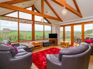 A living room with leather sofas a red rug large windows and wooden beams at Kingcup Cottage in St Columb Major