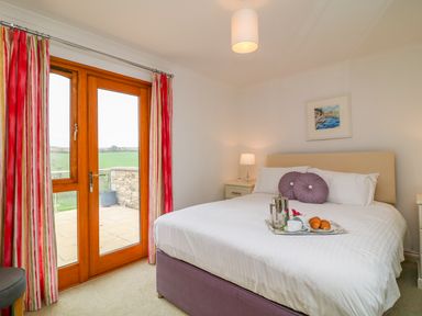 A bedroom with a bed a tray with croissants and tea red and white striped curtains and a door leading outside at Kingcup Cottage in St Columb Major