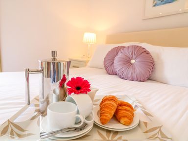 A breakfast tray with a coffee pot cups a flower and croissants on a bed with round pillows at Kingcup Cottage in St Columb Major