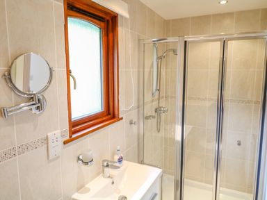 A bathroom with a sink a round wall mirror a window and a shower cabin at Kingcup Cottage in St Columb Major