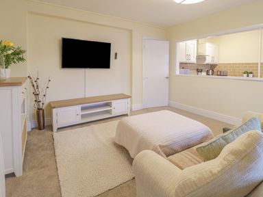 A living room with a wall mounted tv a cabinet a white door and a window to the kitchen at Beside The Sea - In Town in Llandudno