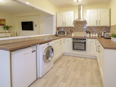 A kitchen with white cabinets a washing machine microwave oven and toaster at Beside The Sea - In Town in Llandudno