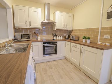 A kitchen with white cabinets wooden countertops a stainless steel sink an oven a microwave a toaster and plants at Beside The Sea - In Town in Llandudno