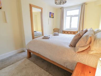 A bedroom with a double bed pillows towels a wooden chair a mirror and a window at Beside The Sea - In Town in Llandudno