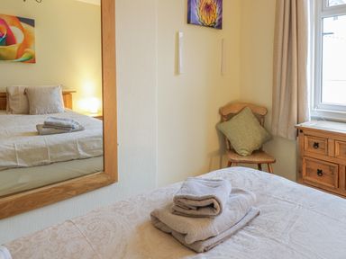 A bedroom with a bed with folded towels on it a wooden chair with a cushion a wooden dresser and a window at Beside The Sea - In Town in Llandudno