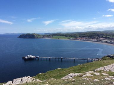 A coastal landscape with a long pier extending into the sea and a town along the shoreline at Beside The Sea - In Town in Llandudno