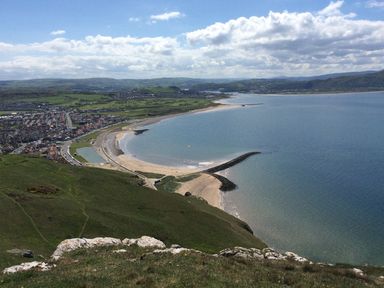 A coastal town with a sandy beach and sea with a breakwater and green hills at Beside The Sea - In Town in Llandudno