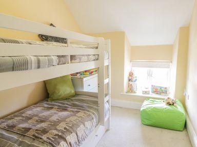 A small bedroom with bunk beds toys on windowsill and a green bean bag at Angorfa in Llanbedr