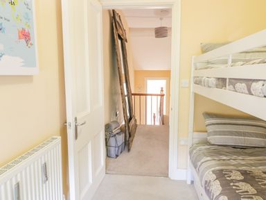 A bedroom with bunk beds next to a door opening to a hallway with a wooden framed mirror and rolled rugs leaning against the wall at Angorfa in Llanbedr
