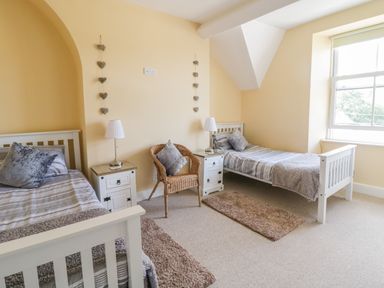A bedroom with two single beds each with a bedside table and lamp and a wicker chair between the beds at Angorfa in Llanbedr
