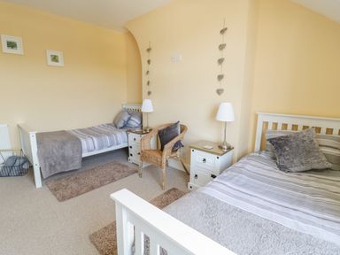 A bedroom with two single beds two bedside tables with lamps a wicker chair and wall decorations at Angorfa in Llanbedr