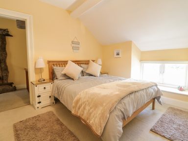 A bedroom with a wooden bed frame bedside tables lamps two rugs and a window at Angorfa in Llanbedr