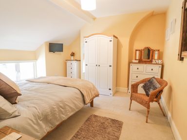 A bedroom with a bed a wardrobe a chest of drawers a wicker chair and a wall-mounted TV at Angorfa in Llanbedr