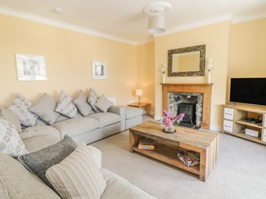A living room with sofas pillows a wooden coffee table with flowers a fireplace and a television at Angorfa in Llanbedr