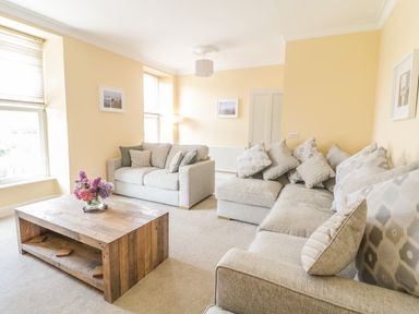 A living room with two sofas a wooden coffee table with flowers and light yellow walls at Angorfa in Llanbedr