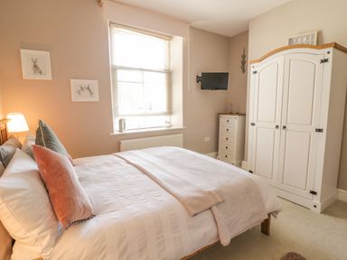 A bedroom with a bed pillows lamp window wardrobe and dresser at Angorfa in Llanbedr