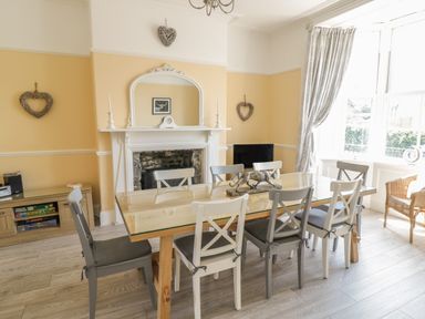 A dining room with a wooden table and chairs near a fireplace and window at Angorfa in Llanbedr
