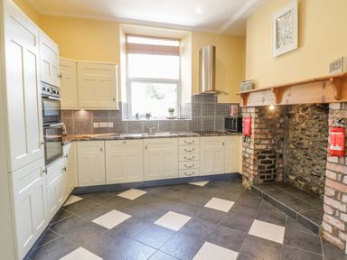 A kitchen with white cabinets black and white tiled floor and a stone fireplace at Angorfa in Llanbedr