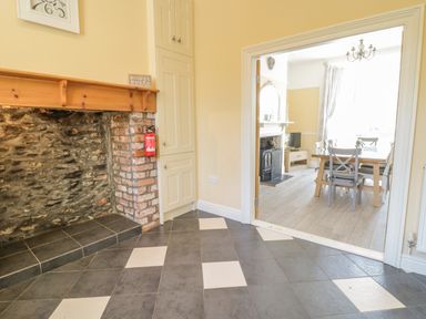 An empty room with tiled floor and a fireplace opening next to a built in cupboard leading to a dining area with a table and chairs at Angorfa in Llanbedr