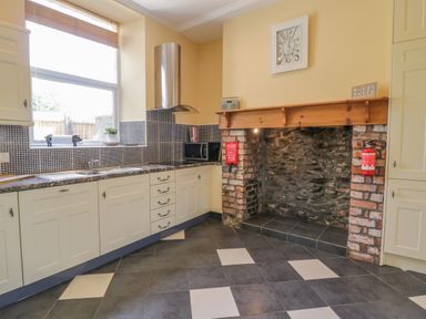 A kitchen with white cabinets a window above the sink a microwave and an exposed brick fireplace at Angorfa in Llanbedr