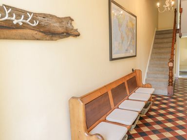 A hallway with a wooden bench and cushions a staircase and a world map on the wall at Angorfa in Llanbedr