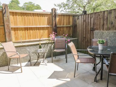 An outdoor patio with chairs a small table with a bottle and glasses and a glass dining table with a plant at Angorfa in Llanbedr