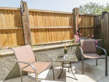 A small outdoor seating area with two chairs a glass table and a bottle with glasses at Angorfa in Llanbedr