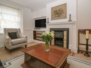A living room with an armchair a wooden coffee table with a flower vase a fireplace and a TV at Dolphin House in Burford