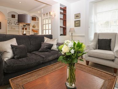 A living room with a dark sofa and light armchair and flowers on a wooden coffee table at Dolphin House in Burford