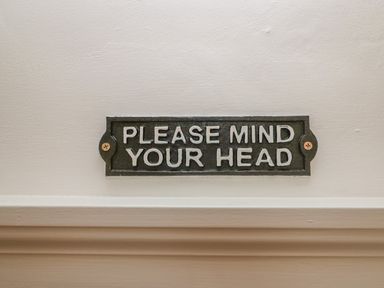A metal sign on a wall that reads Please mind your head at Dolphin House in Burford