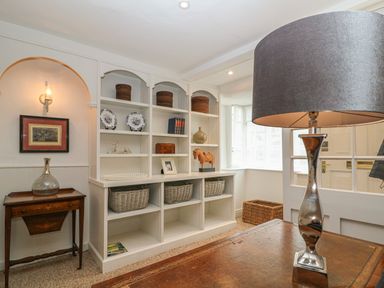 A room with white built in shelves holding decorative items a wooden side table with a glass vase and a table lamp on a wooden surface at Dolphin House in Burford