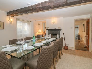 A dining room with a glass table set for eight and a black fireplace at Dolphin House in Burford